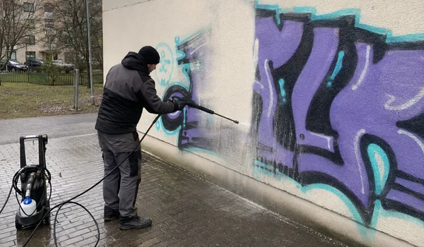 Grafiti eemaldamine fassaadilt, meister peseb survepesuriga lillat grafitit krohvitud seinalt, lahustigeel kantakse 5 sentimeetri laiuselt ka grafiti ümber, kuhu pihustivärvi peen udu on jõudnud.