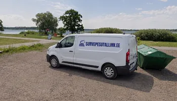 Valge kaubik survepesutallinn.ee kirjaga Maardu järve kaldal kruusaplatsil, taga roheline konteiner ja järv, objektil pargitakse kaubik tagaustega pesuala poole, sest pesur ja voolikurull tulevad välja tagaustest.