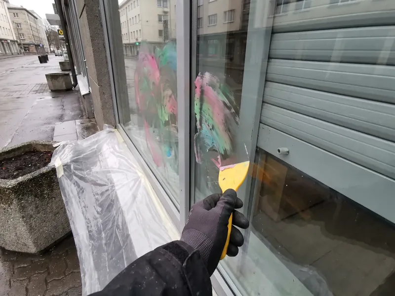Kindas käsi kaabib kollase plastkaabitsaga poe vaateaknalt laiali lahustunud värvilaike, kõnnitee lillekast on kaetud kilega ja kõrval on hall rulluks, klaasi hoitakse kaapimise ajal pidevalt märjana, et kaabits libiseks kriimustamata.