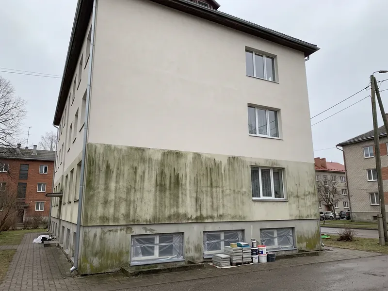 Kolmekorruselise korterelamu krohvitud sein halli taeva all, ülemised korrused on pestud heledaks ja alumise korruse krohvil on veel roheline vetikavöö, keldriaknad on kilega kaetud, vetikavöö kasvab seinal sinna, kuhu vihmavesi sillutiselt tagasi pritsib.