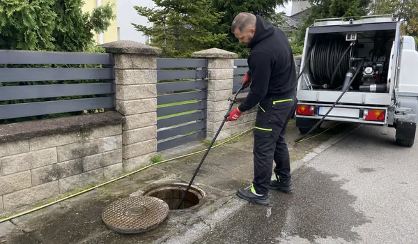 Ummistuse kõrvaldamine survepesuga, meister laseb voolikut piirdeaia ääres avatud kaevu, taga voolikurulliga hooldusauto, keeva vee valamine rasvaummistust ei lahenda, rasv tardub torus uuesti.